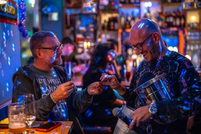 Torsten Poggenpohl (rechts) im Gespräch bei einem Charity-Abend in Hamburg, stimmungsvolle Atmosphäre mit Getränken und Publikum im Hintergrund.