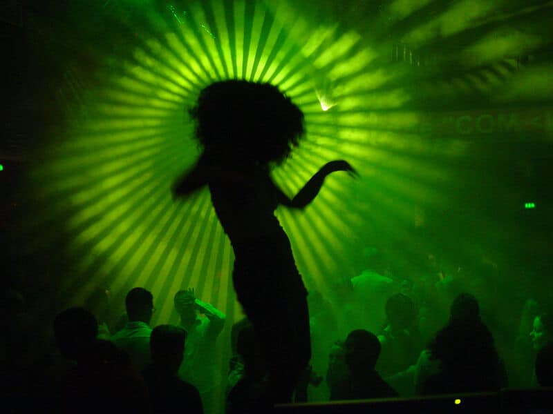 Silhouette einer tanzenden Person auf einer Clubtanzfläche mit grünem Licht im Hintergrund.