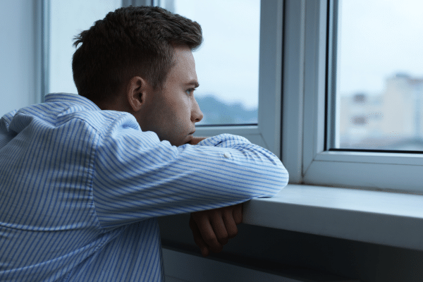 Mann blickt nachdenklich aus dem Fenster – Symbolbild für Ausgrenzung und Diskriminierung von Menschen mit HIV