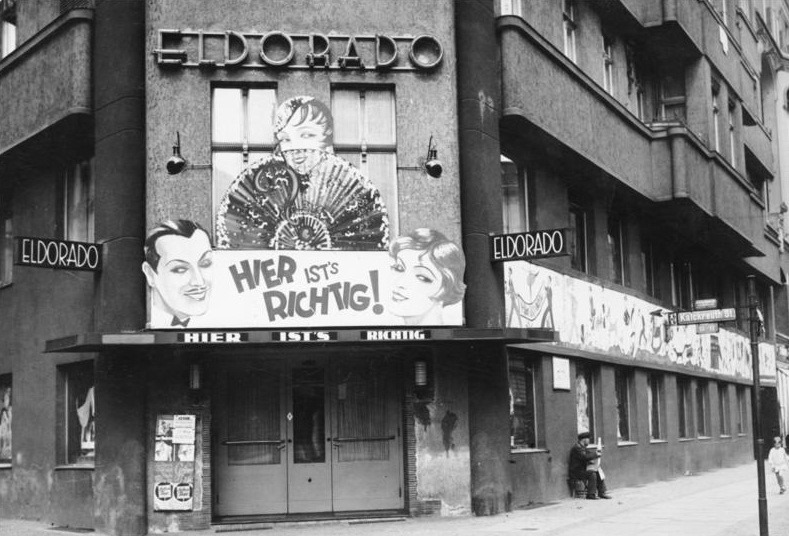 Foto der Außenwand des Eldorados, einem queeren Nachtclub im Berlin der 1920er Jahre. Man sieht zwei Personen in der Kleidung des jeweils anderen Geschlechts. Unter dem Schriftzug "Eldorado" steht "Hier ist's richtig!"