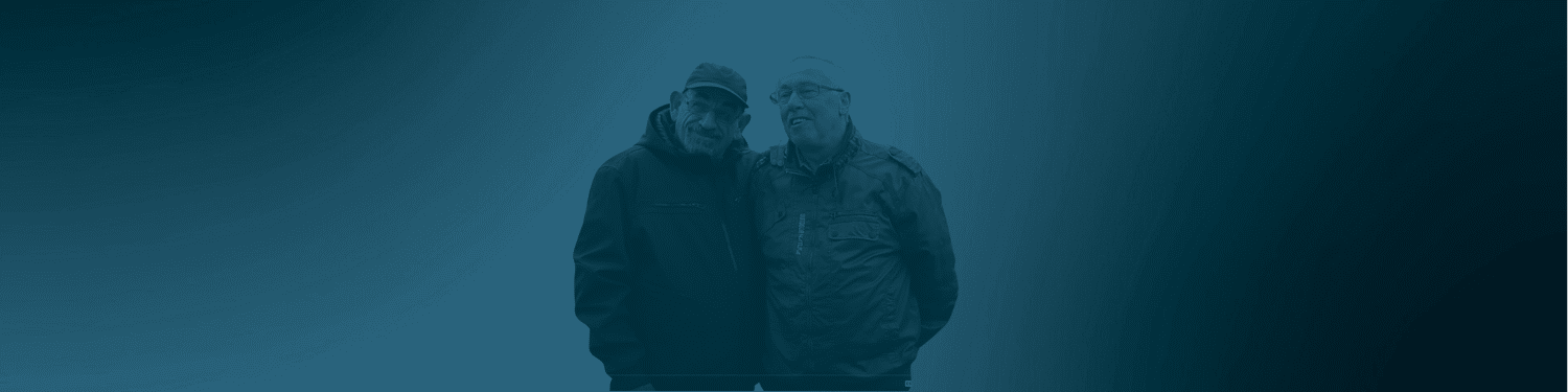 Guido und sein Partner stehen eng beieinander vor dunklem blaugrünem Hintergrund.