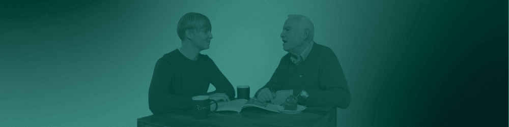 Zwei Männer aus unterschiedlichen Generationen sitzen an einem Tisch und sprechen miteinander.